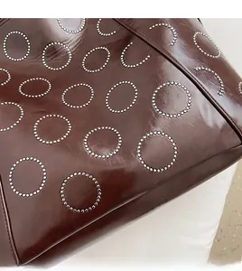 Detail view of dark brown waxed leather bag with silver rivet circles and stitching