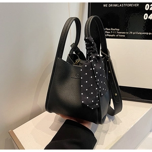 Close-up of black litchi texture bucket bag with polka dot scarf and double handles