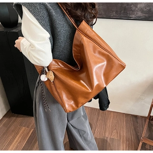 Detail view of a large caramel brown faux leather tote bag with a baseball charm hanging