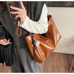 Close-up of caramel leather tote bag with soft texture and white baseball charm detail