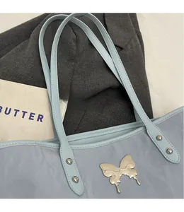 Detail of light blue tote bag with silver butterfly emblem and metal studs on shoulder strap
