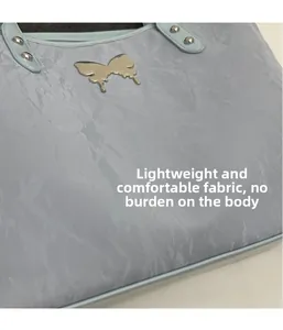 Detail of light blue tote bag featuring pleated fabric texture and silver butterfly ornament