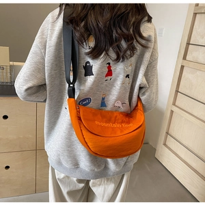 Detail of orange nylon crossbody bag with mountain line embroidery on a model
