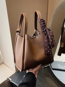 Chic brown leather bucket bag with top handles and a polka dot silk scarf detail