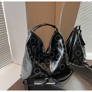 Detail of a black glossy tote with silver metal rivets in hollow circular patterns