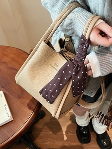 Khaki leather bucket bag with silk scarf detail and embossed logo on wood table