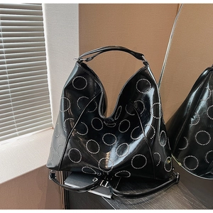 Detail view of large black glossy tote bag with silver rivet circles and handle