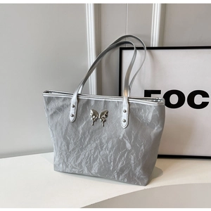 Close-up of silver tote bag featuring crinkled texture and metallic butterfly emblem