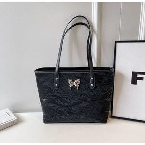 Detail of black wrinkled texture tote bag featuring a silver metal butterfly ornament