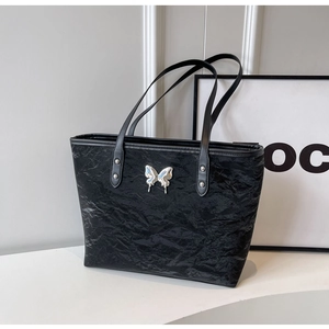 Detail of black wrinkled texture tote bag featuring a silver butterfly metal ornament