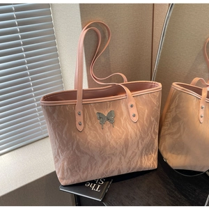 Detail of pink tote bag with ruched texture and metallic liquid butterfly emblem