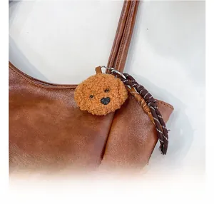 Dettaglio di un simpatico ciondolo a forma di cane in peluche marrone su una borsa vintage
