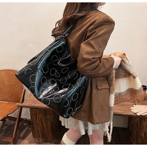 Detail of a large black leather tote bag with white circular patterns and a shoulder strap