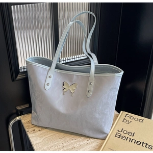 Detail view of light blue tote bag with pleated texture and silver butterfly pendant charm