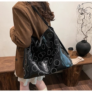 Detail of black glossy tote bag with silver rivet circles shown in a cozy indoor setting