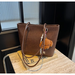 Dettaglio borsa tote in pelle marrone scuro con ciondolo di peluche e nastro sui libri
