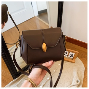 Detail of dark brown leather crossbody bag featuring a gold oval clasp and slim strap