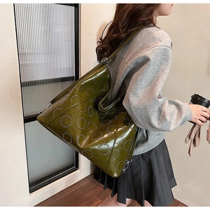 Detail view of large olive green tote bag featuring circular rivet design and glossy leather
