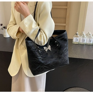 Detail of a large black tote bag featuring a silver butterfly pendant and pleated texture