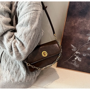 Retro brown PU leather shoulder bag with gold clasp and chain detail on grey sweater