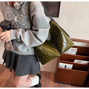 Detail of olive green leather shoulder bag with circular metal rivet patterns and wide strap