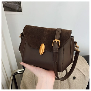 Detailed close-up of dark brown leather crossbody bag with suede flap and gold metal clasp