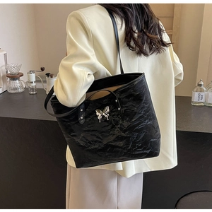 Detail showing metallic butterfly charm on black wrinkled leather tote bag with long straps