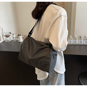 Détail du sac à bandoulière en nylon gris foncé avec large sangle et logo métallique