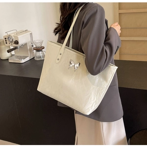 Macro shot of large beige patent leather tote bag featuring a silver butterfly metallic logo