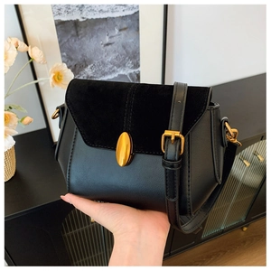 Detail of black crossbody bag featuring suede patchwork and gold oval metal lock