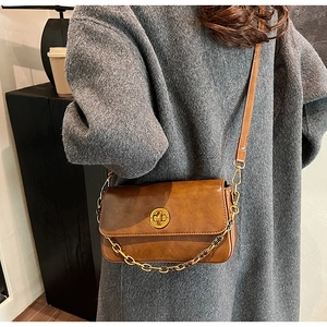 Brown vintage leather bag with gold chain strap shown on a dark grey wool coat