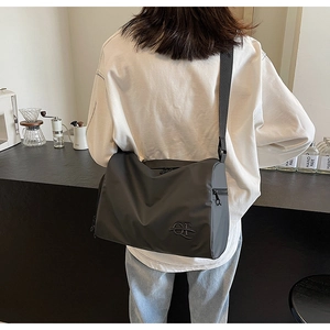 Détail d'un sac cabas gris foncé avec logo métallique et sangle sur l'épaule