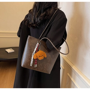 Dettaglio della borsa tote in pelle marrone scuro con ciondolo a cane di peluche sulla spalla
