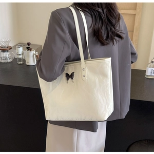 Detail of off-white tote bag with black butterfly charm shown on a shoulder