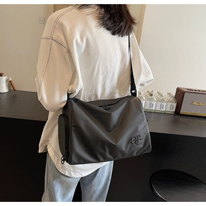 Vue latérale du sac en nylon noir avec poche zippée et détail du logo QE en métal