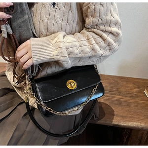Detail of black leather crossbody bag with golden chain and metallic twist-lock closure