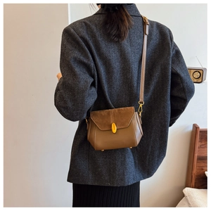Detail of a brown vintage square bag featuring suede texture and gold oval metal clasp