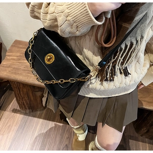 Close-up of black crossbody bag with gold chain and clasp on a knit sweater outfit