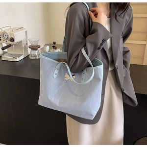 Detail of light blue tote bag featuring embossed texture and a silver butterfly charm