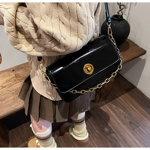 Detail of glossy black leather crossbody bag with gold round clasp and chain strap