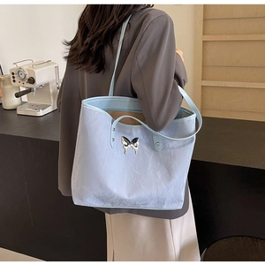 Close-up of light blue tote bag with silver butterfly charm and pleated texture detail