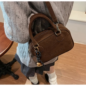 Detalle de bolso MEDEAR en ante marrón con logo grabado y colgante de raqueta de tenis
