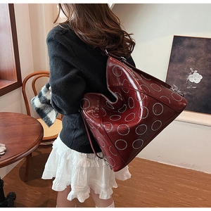 Detailed view of burgundy leather tote bag featuring circular silver rivet embellishments