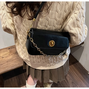 Chic black crossbody bag with gold round lock and metal chain shown on model in a cozy setting