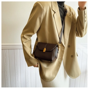 Detail of dark brown leather crossbody bag featuring a vintage gold clasp on model