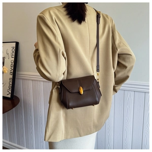 Detail showing vintage brown leather crossbody bag with golden leaf buckle on a beige suit