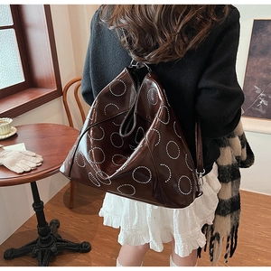 Detail of dark brown leather tote bag with white rivet circles and silver metal hooks