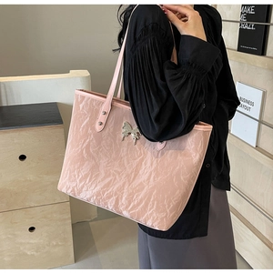 Detail of pink pleated tote bag featuring a metallic butterfly charm and shoulder straps