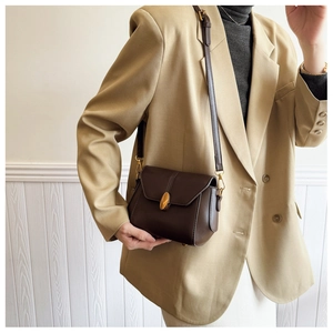 Detail of dark brown leather crossbody bag with oval gold clasp on khaki blazer