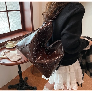 Detail of large dark brown patent leather tote bag with stylish white rivet circle pattern